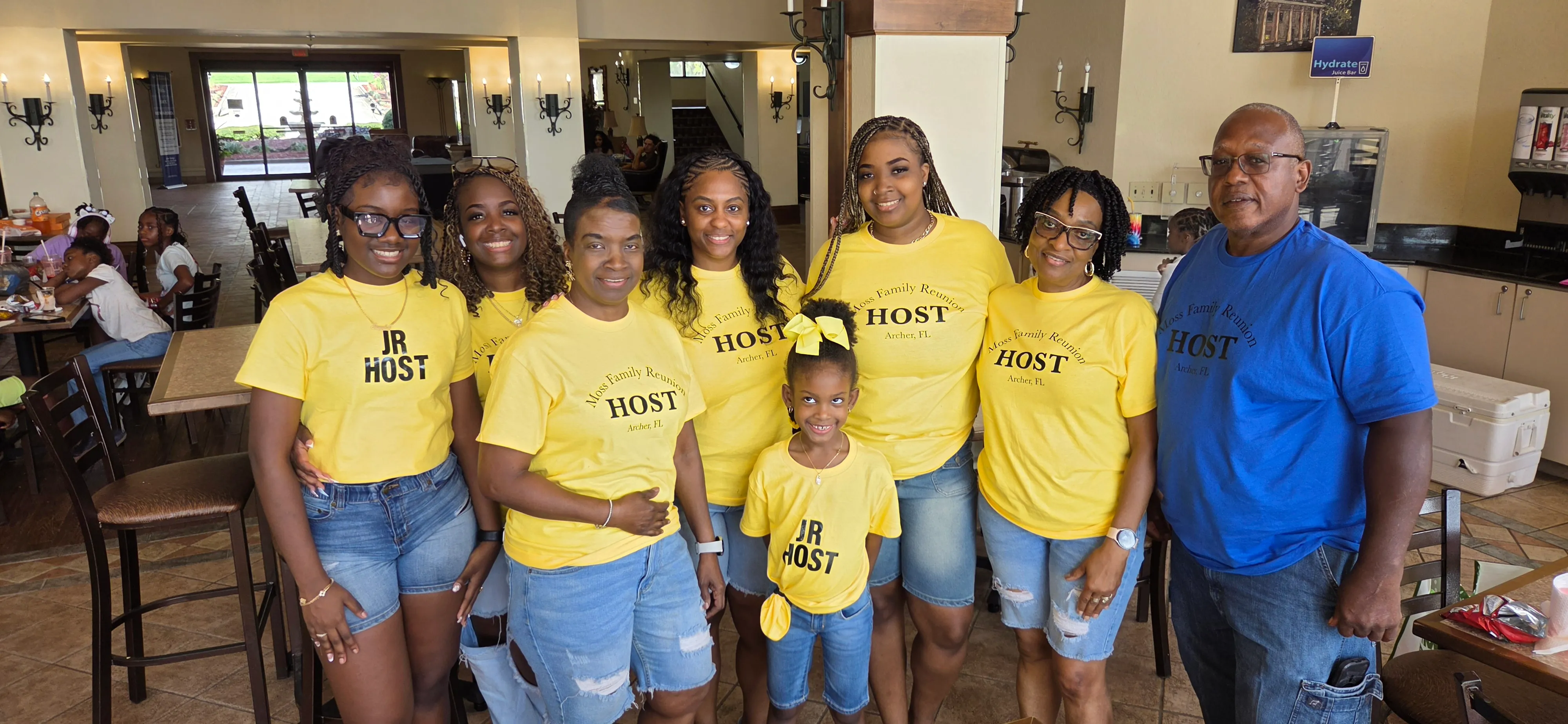 Women, a young girl and a man in a blue shirt smiling together, most wearing yellow HOST t-shirts.