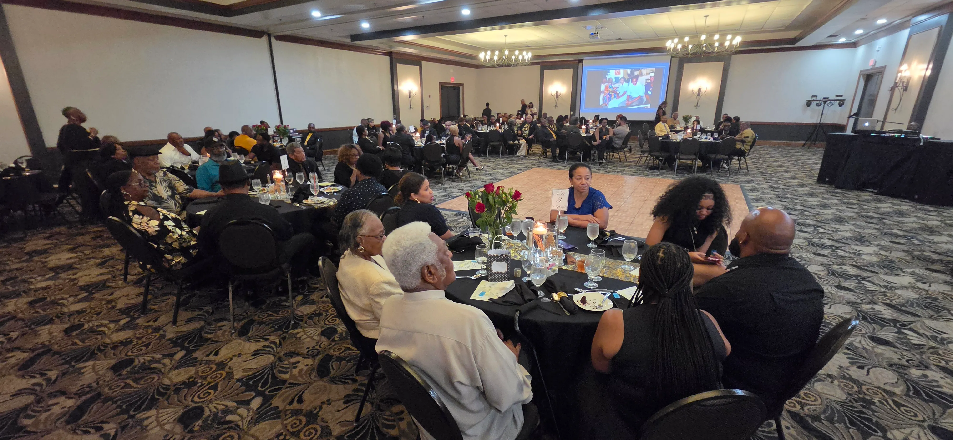 A wide view of the banquet hall with family seated at round tables.