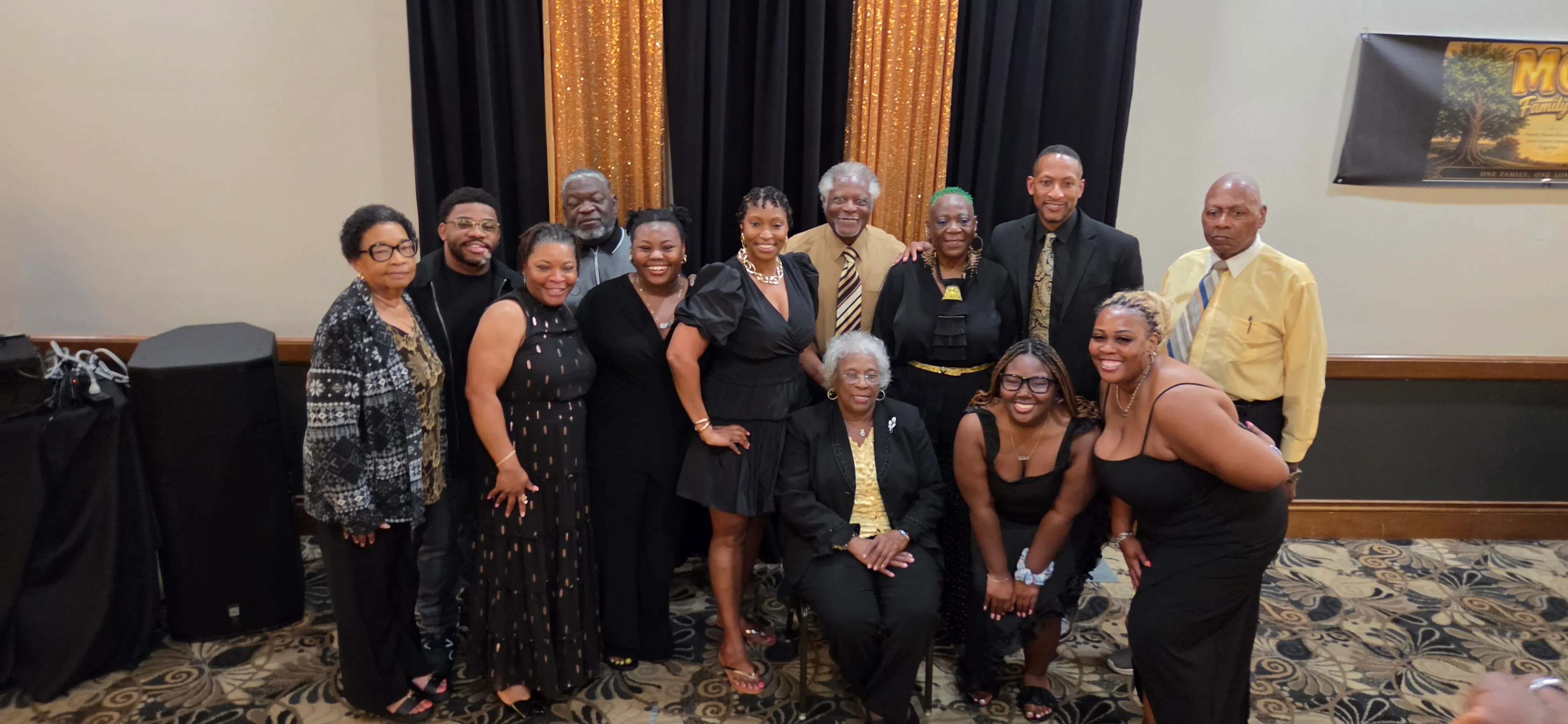 A group in dressy black outfits posing in the banquet hall, some seated in front.